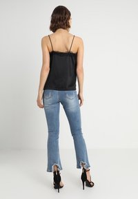 Camisón de satén negro con encaje, combinado con jeans acampanados desgastados en azul claro y sandalias de tacón alto negras. Vista trasera.