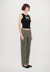 Juodas raukšlėtas rankovių viršus su "Moschino Jeans" logotipu, derinamas su alyvuogių žalios tiesaus kirpimo džinsais, kuriuose yra smėlio spalvos detalė, ir plokščiais juodais bateliais.