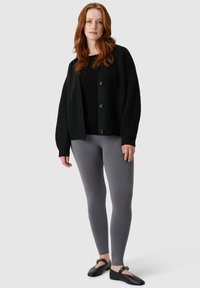 Czarny dzianinowy kardigan z guzikami, noszony na czarną bluzkę i szare legginsy; wykończony czarnymi płaskimi butami. Charakteryzuje się teksturowanym wzorem dzianiny.