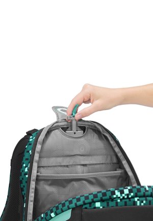 Hand passt den Teleskopgriff in einem teilweise geöffneten, grau-türkisfarbenen Rucksack mit pixelartigem Muster an.