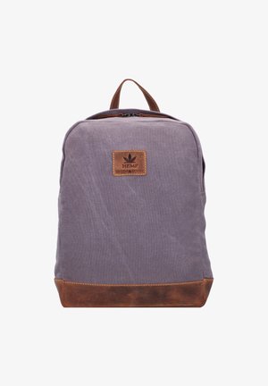 Mochila de lona morada con fondo y acentos de cuero marrón. Presenta una forma rectangular y un asa superior, con un parche de logo en la parte delantera.