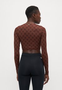 Brun langermet crop topp med blomstermønster, jevn tekstur og logo på baksiden. Kombinert med svarte high-waisted leggings.