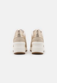 Beige Sneakers mit metallischen Akzenten, weicher Textur, weißer Sohle und dickem Absatz. Mit einer glatten Oberfläche und dezentem Branding gestaltet.