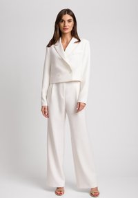 Biała krótka marynarka z podwójnymi guzikami i jedną kieszenią na piersi, zestawiona z szerokimi spodniami. Gładki materiał o czystym wykończeniu.