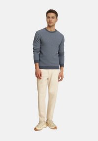 Geweven blauwe trui met een ronde halslijn, gecombineerd met crèmekleurige broeken en lichte sneakers. Eenvoudig ontwerp en een aansluitende stijl.