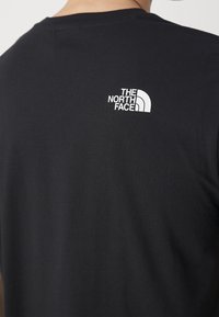 Černé tričko na osobě, na horní části zad blízko výstřihu se nachází malé bílé logo "The North Face".