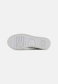 White athletic shoe outsole with textured tread and two circular accents. Smooth material with ridges and grooves for traction.