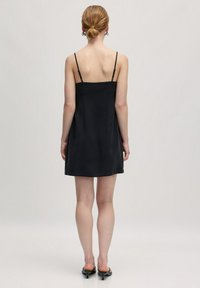 Schwarzes Slipkleid mit verstellbaren dünnen Trägern, glatter Textur und einer lockeren A-Linie. Der Saum endet über dem Knie.