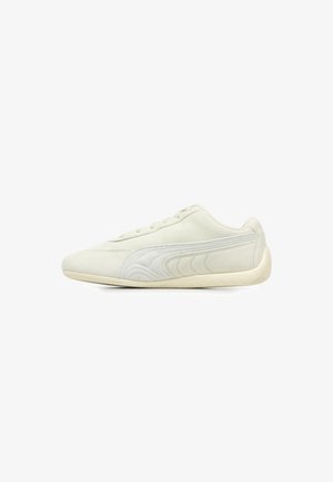 Zapatilla deportiva gris claro hecha de ante, con una superficie suave, punta redonda, diseño minimalista, cierre de cordones en la parte delantera y acentos texturizados en los laterales.