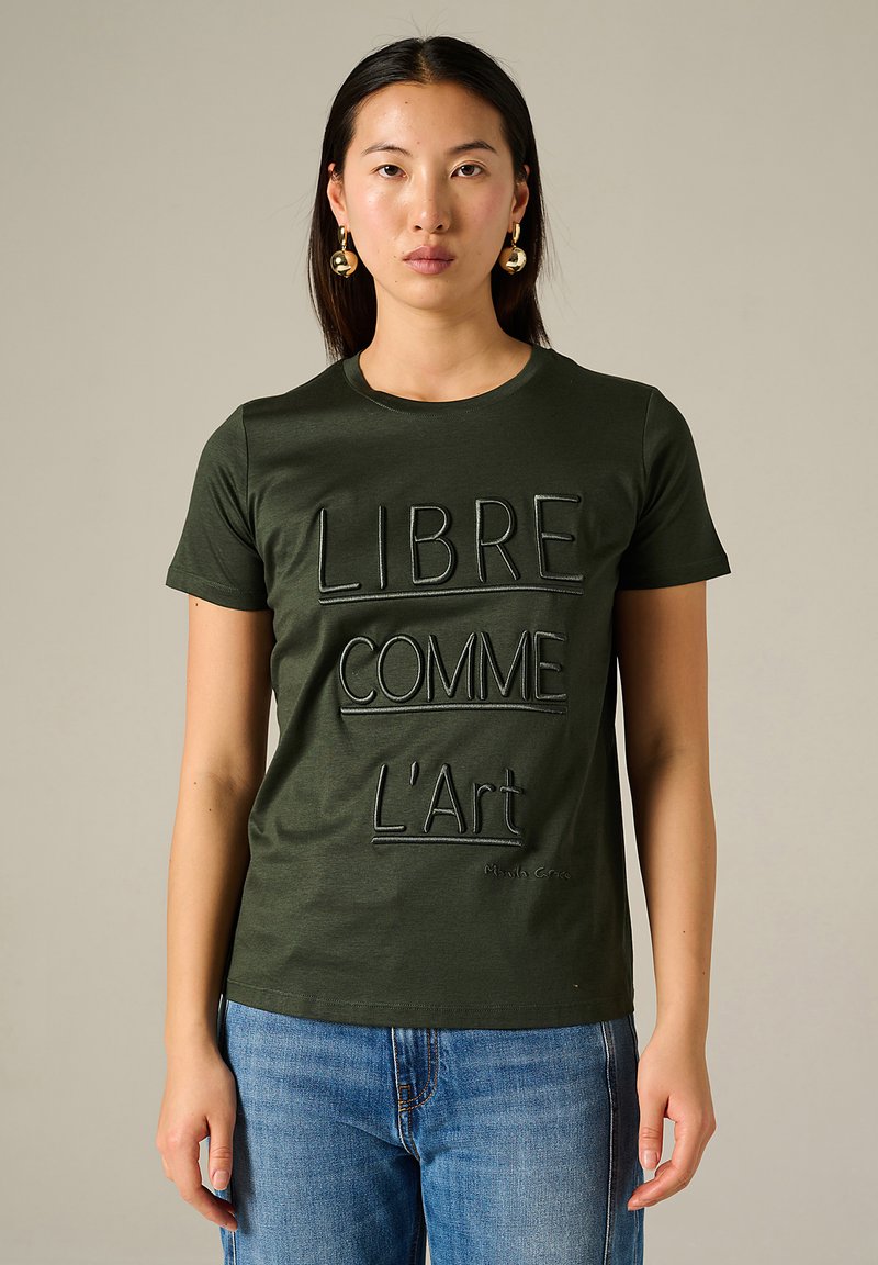 T-shirt en coton vert olive à manches courtes avec broderie du texte "LIBRE COMME L'Art" en noir. Encolure ronde, coupe décontractée.