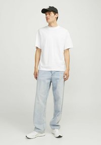 Hvid kortærmet t-shirt parret med lyseblå løse jeans og hvide sneakers, suppleret med en sort kasket. Enkel og afslappet stil.