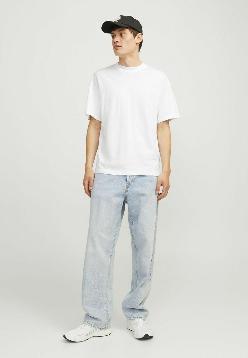 Hvid kortærmet t-shirt parret med lyseblå løse jeans og hvide sneakers, suppleret med en sort kasket. Enkel og afslappet stil.