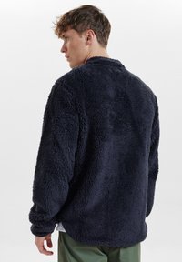 Felpa blu navy in pile, con un taglio morbido e rilassato, dotata di maniche lunghe e una superficie morbida e testurizzata.