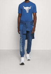Blauwe katoenen t-shirt met een stierafbeelding, gecombineerd met bijpassende blauwe joggers met witte tekst. Witte sneakers maken de outfit compleet.