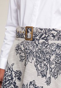 Floral-patterned fabric skirt with a beige and navy color scheme. Features a textured weave and a rectangular gold buckle on the belt.