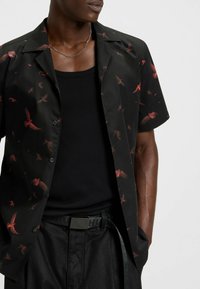 Zwart overhemd met korte mouwen, voorzien van een rode vogelprint, gemaakt van gladde stof, met een open kraag en zwarte knopen, gecombineerd met een zwarte tanktop en een riem.