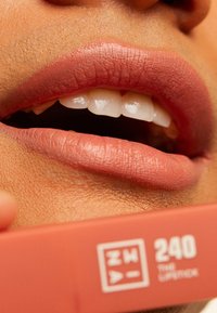 Lipstickrør merket "240" i en myk terrakottafarge ved siden av et nærbilde av fyldige lepper med en matt finish og en naturlig rosa nyanse.