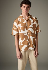 Trumpomis rankovėmis, apykaklės marškiniai smėlio ir baltos spalvos, su abstrakčiais raštais. Pagaminti iš lengvos medžiagos, su sagomis priekyje.