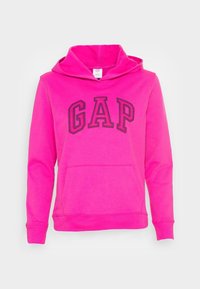 Sudadera fucsia de tela suave que presenta un gran logo "GAP" en negro. Tiene un bolsillo frontal y una capucha con cordón.