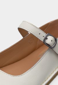 Λευκό δερμάτινο παπούτσι Mary Jane με ρυθμιζόμενο λουράκι ασημί αγκράφα και ταμπά επενδυτική επένδυση με μαξιλάρι.