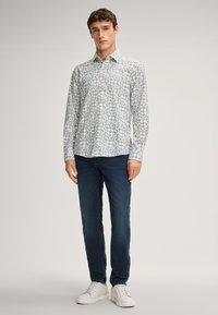  Lichtgrijze overhemd met een geometrisch patroon in donkergrijs. Slim fit, lange mouwen, gecombineerd met donkere denim en witte sneakers.