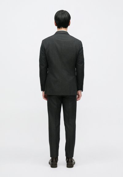 Tamnosivi prugasti odijelo s prilagođenim krojem, koje uključuje jaknu s jednim prorezom, hlače ravnih nogavica i kožne čizme.