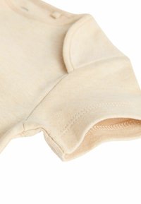 Ljust beige bomullsbody med korta ärmar, som har en mjuk textur, rundad halsringning och tryckknappar vid axeln.