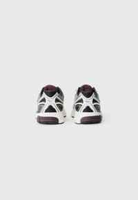 Sport sneakers med en overdel i sort, hvid og grå mesh, lilla accenter på hælen og en tekstureret gummisål. Set fra bagsiden.