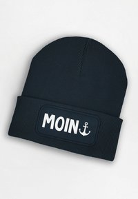 Navy knitted beanie with a folded cuff, featuring a rectangular patch that displays the text "MOIN" and an anchor icon in white.