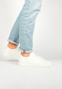 Baskets en cuir blanc avec un embout texturé, lacets plats et semelle en caoutchouc épaisse. Portées avec un jean light blue retroussé.