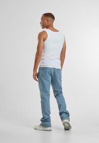 Balta be rankovių marškinėliai ir šviesiai mėlynos džinsai. Modelis matomas iš nugaros, vilkintis šviesios spalvos sportinius batelius. Paprastas, kasdienis drabužis.