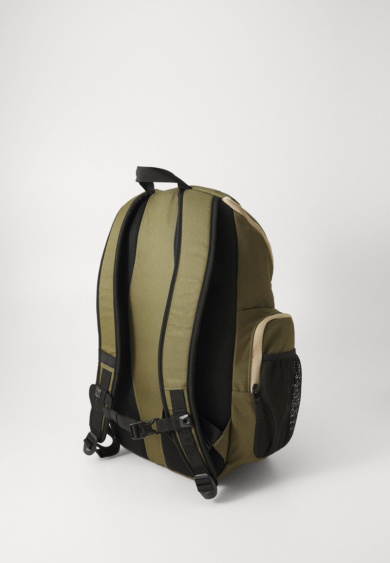 Zaino verde oliva con accenti in rete nera, spalline imbottite, due tasche laterali e una maniglia superiore per un facile trasporto. Costruzione in tessuto resistente.