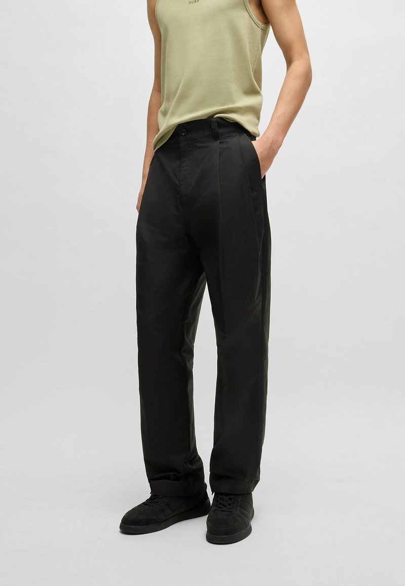 Pantalons larges noirs à texture lisse, avec poches avant, passants de ceinture et coupe droite. Associés à un débardeur vert olive.
