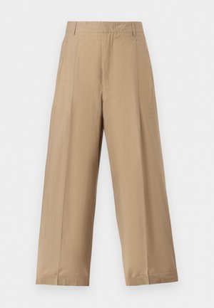 Pantalon beige à jambes larges avec pli frontal, passants pour ceinture et poches latérales, conçu pour une coupe décontractée.