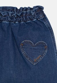 Tissu en denim bleu foncé avec une taille élastique et une poche en forme de c�œur cousue sur le côté droit.