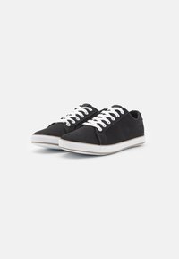 Zapatillas de lona negras con cordones blancos, diseño de corte bajo, puntera redonda y suela blanca. Presentan costuras mínimas y una superficie texturizada.