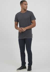 Czarnoszary bawełniany t-shirt z krótkim rękawem, okrągłym dekoltem i dopasowanym krojem, w zestawieniu z granatowymi spodniami slim fit oraz czarnymi sneakerami.
