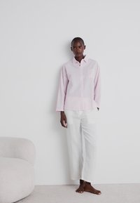 Ανοιχτό ροζ καρό πουκάμισο με γιακά και μπροστινή τσέπη, συνδυασμένο με λευκά παντελόνια φαρδιάς γραμμής. Μαλακές υφές, μινιμαλιστικός σχεδιασμός.