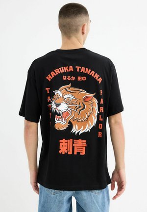 Camiseta de algodón negra con un gran gráfico de un tigre rugiente en naranja y blanco, con texto y acentos en rojo. Corte casual.