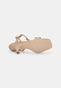 Beige sandálky na vysokém podpatku s hladkým povrchem, tenkými pásky, zlatými akcenty a kulatou špičkou. Čtvercový podpatek poskytuje stabilitu.