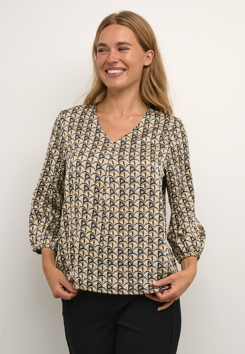 Patterned blouse with a V-neck, black and gold fan design, textured fabric, and puffed, gathered sleeves. Worn with black trousers.