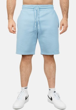 Shorts en coton bleu clair avec une taille élastique et un cordon de serrage, dotés de deux poches latérales et d'une coupe droite. Portés avec des baskets blanches.