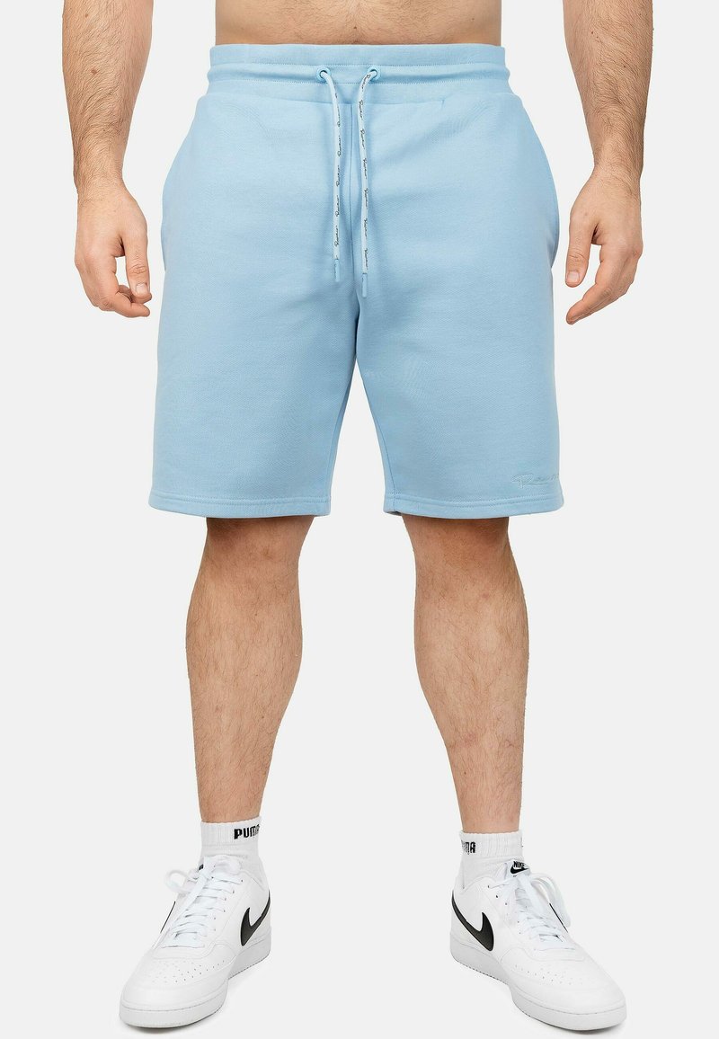 Lichtblauwe katoenen shorts met een elastische tailleband en een trekkoord, voorzien van twee zijzakken en een rechte snit. G gedragen met witte sneakers.