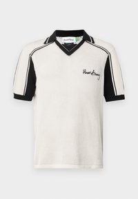 Strikket polo skjorte i krem og svart, med v-hals, korte ermer, kontraststriper og brodert logo på brystet.