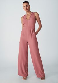 Mouwloze jumpsuit in rozenroze, met een V-hals, wijde broekspijpen, zijzakken en een getailleerde taille. Glad materiaal met een matte afwerking.