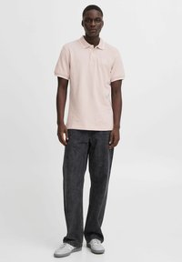 Lyserød polo shirt med klassisk krave, parret med mørkegrå bukser med bred ben og hvide sneakers. Skjorten har et lille logo på brystet.