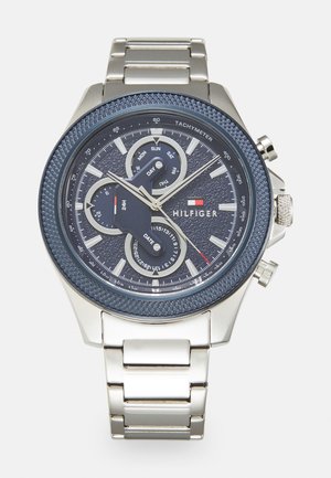 Reloj cronógrafo con un dial texturizado azul marino, pulsera de acero inoxidable plata, taquímetro y dos subdiales para el día y la fecha.