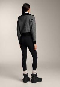 Szary krótki sweter z czarnym prążkowanym dołem, zestawiony z czarnymi legginsami i czarnymi zimowymi butami. Sweter ma duży kołnierz i wzór w kratę.