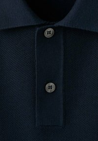 Granatowa koszulka polo o fakturowanym wzorze dzianiny, z trzema guzikami i kontrastującym kołnierzem. Guziki mają kształt okrągły z wypukłym środkiem.