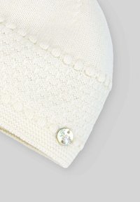 Biała dziana czapka z teksturowanym wzorem, z metką z metallicznym wykończeniem na dolnym brzegu. Miękka, bez widocznych elementów metalowych czy akcentów.